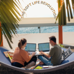 two people working on beach with sign above the soft life revolution