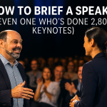 Morris Misel on stage in conversation with an event organiser, smiling with a packed, engaged audience behind them — captured during a live keynote moment.